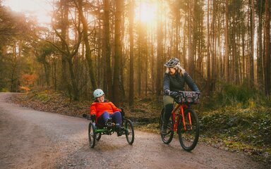 Two women cycling through a forest, one with an adapted bike