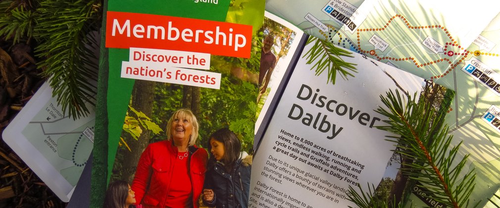 A series of flyers promoting membership at Dalby Forest with a compass and conifer branches placed on top.