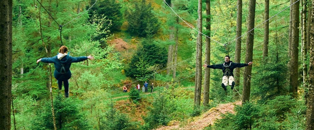 A man and a woman on zip wires through the trees