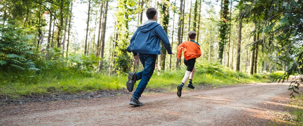 Two boys running along a forest path in the summer.