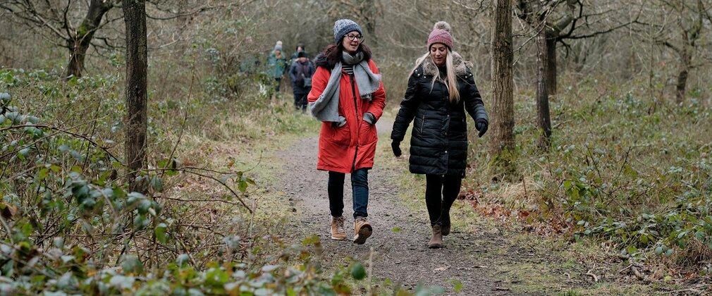 Two women in winter coats, hats and scarves, walking on a forest path.