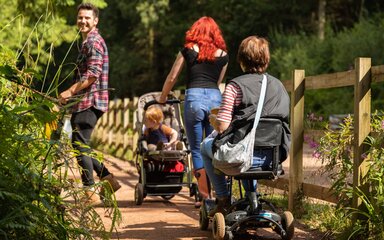 Family walking on a forest path, including a pushchair and a mobility scooter.