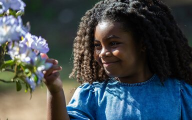 A little girl reaching out to take a closer look at flowers on a tree