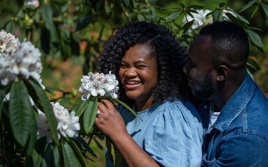 A couple laugh as they take a closer look at a white flower