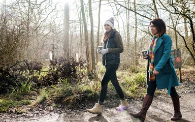 A couple of people walking in the woods holding takeaway coffee cups