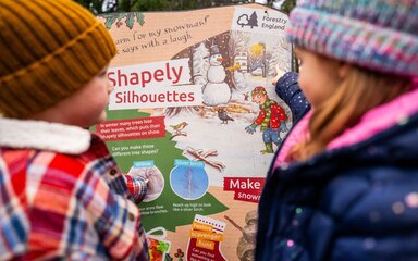 Two children in winter coats and hats looking at a winter-themed Stick Man board.