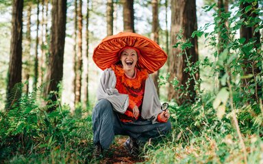 A woman dressed as a mushroom crouched among the trees