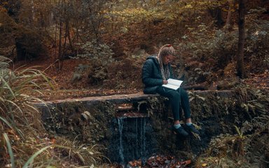 Woman writing in a notepad by a pond
