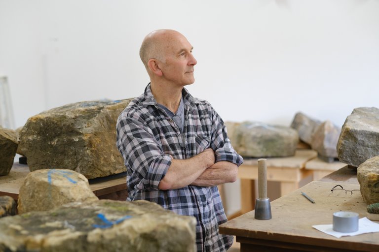 Man stood with folded arms surrounded by giant rocks in a workshop