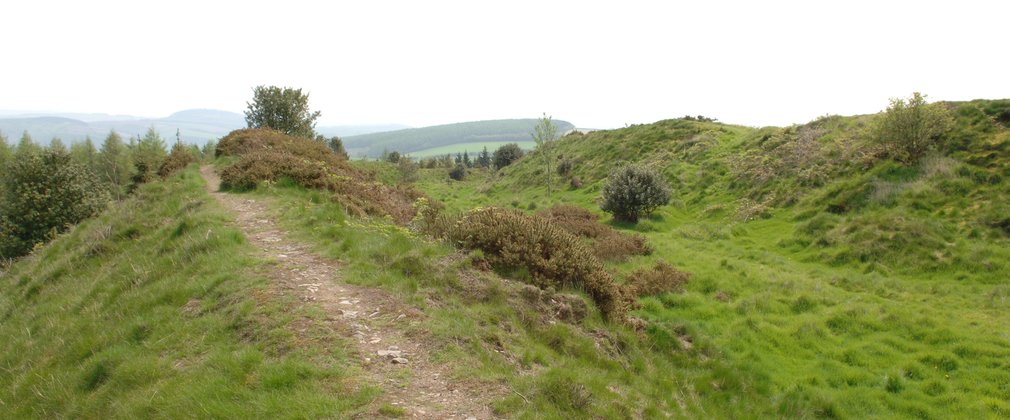 Small unsurfaced walking trail up a hill with rolling hills in the background