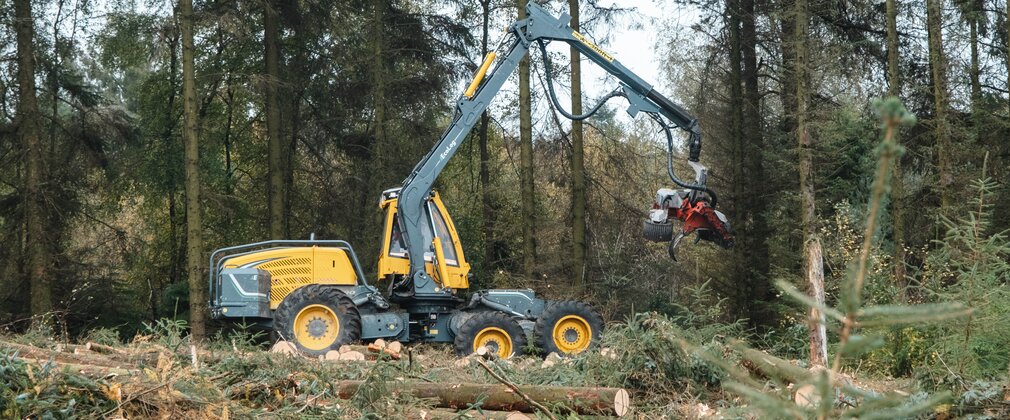 A yellow harvesting machine travelling through a conifer forest