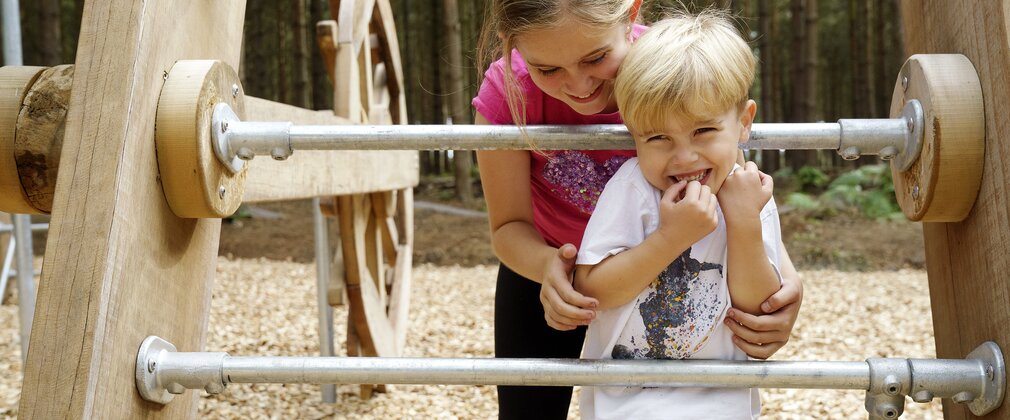 two young children near play equipment in a forest