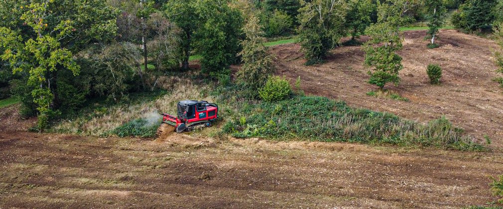 A large forestry machine called a mulcher churns up vegetation on the ground leaving behind brown soil. 