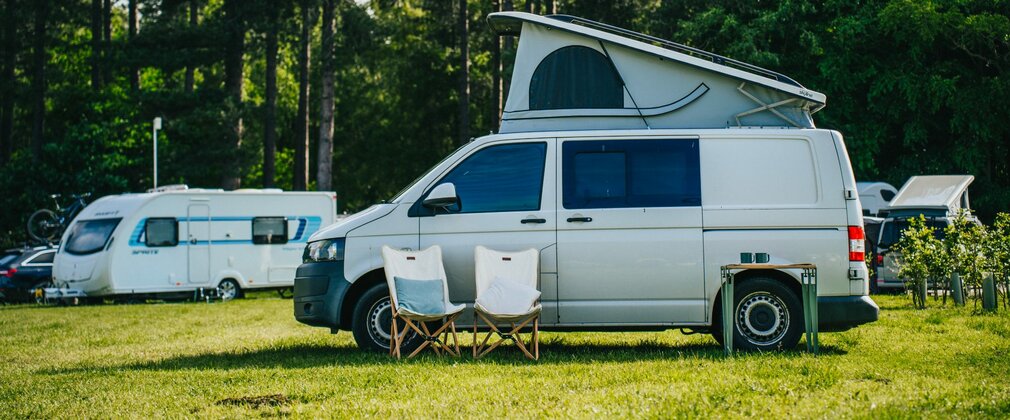 A silver campervan with its roof popped parked up in a forest setting.