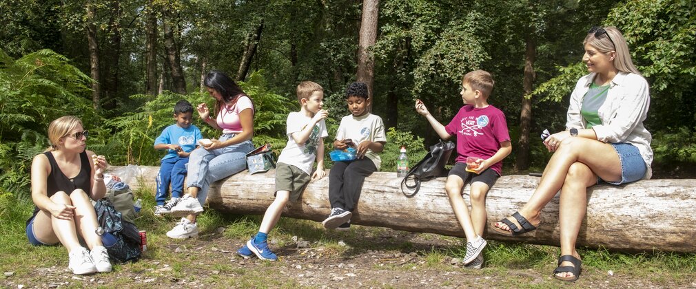 Adults and children sit on a large log having a picnic