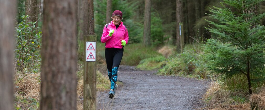 A woman in running clothes and a pink hat running along a forest path in winter