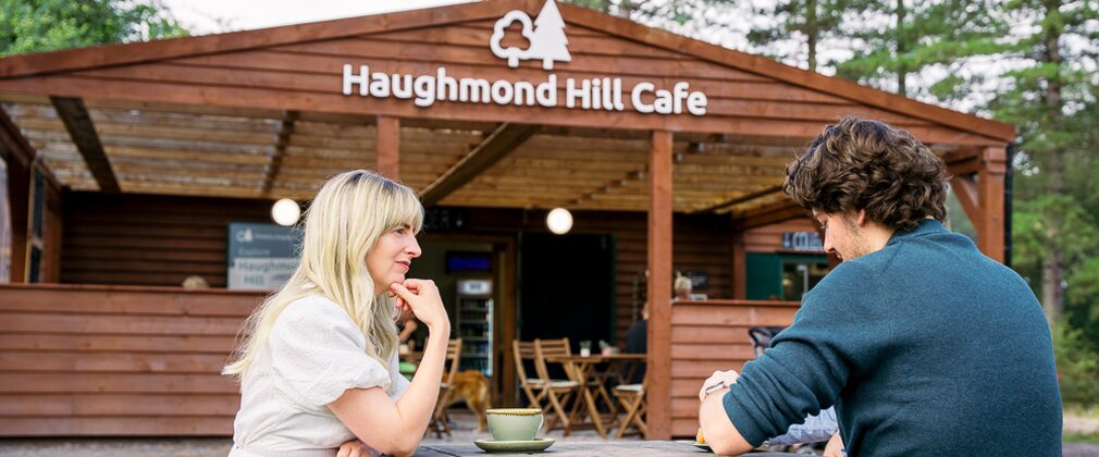 A couple enjoying a hot drink on a wooden bench outside of Haughmond Hill Cafe
