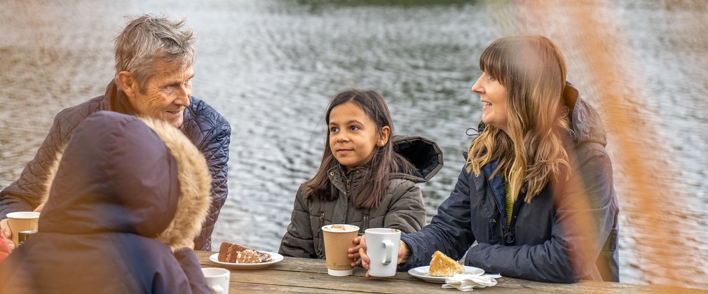 A family sitting next to a lake enjoying tea and cake at Bedgebury Cafe