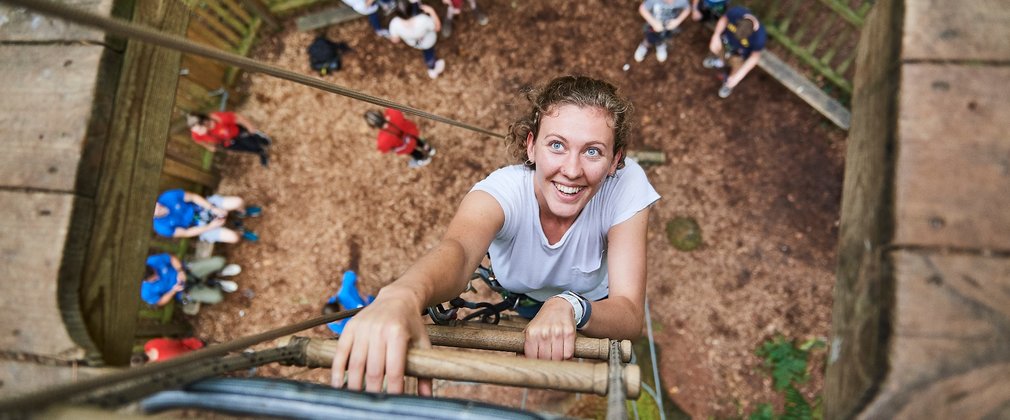 Woman climbs a rope ladder at go ape tree top adventure high lodge