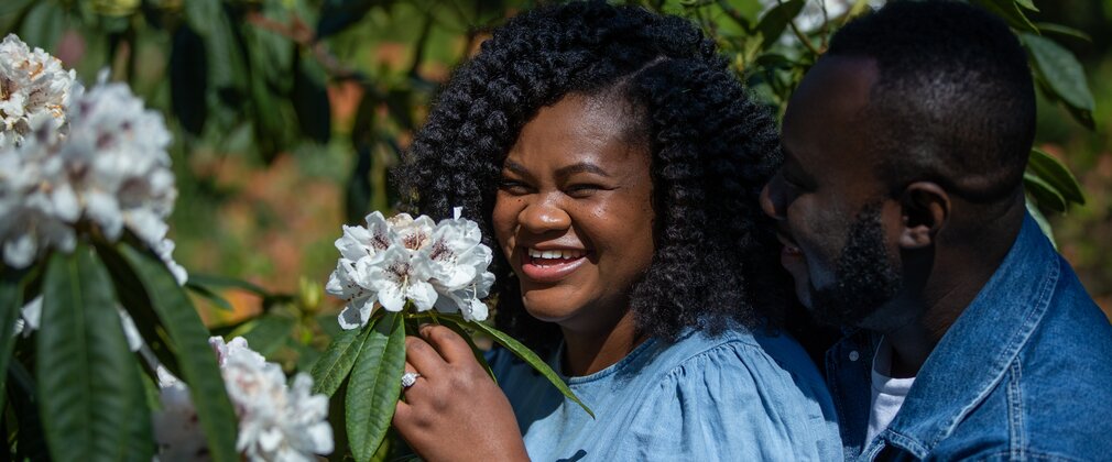 A couple laugh as they take a closer look at a white flower
