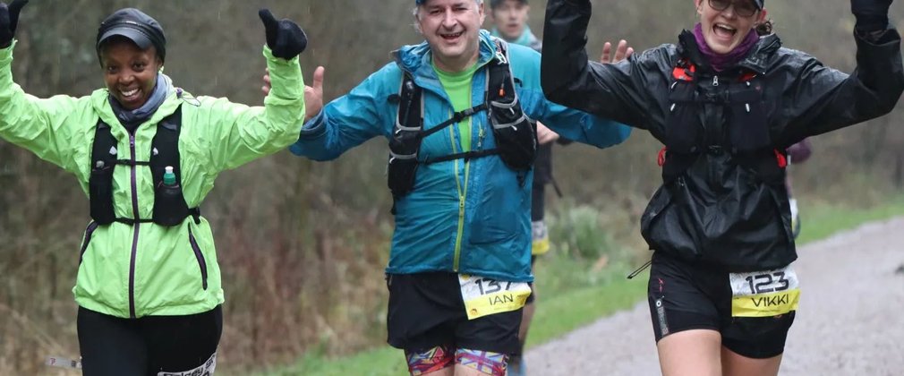 3 people smiling and running in the forest, in wet conditions