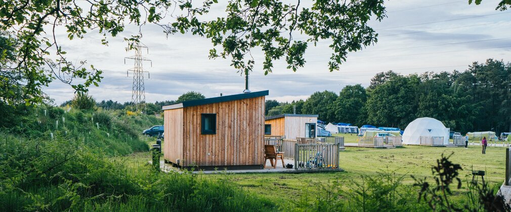 Wooden glamping pod and white geodome at campsite