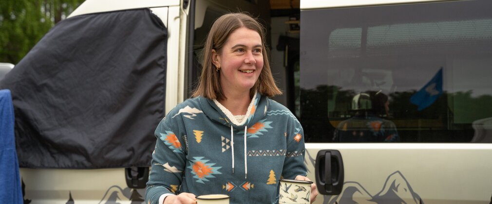 Woman carrying two mugs of tea from a campervan