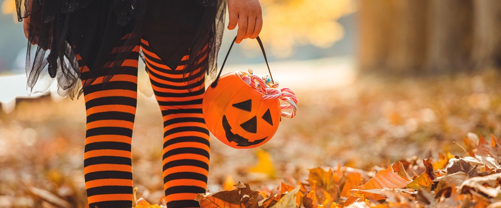 child in stripy orange tights walking through autumn leaves with a pumpkin