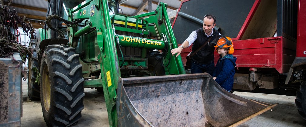 A dad and young boy stand by a large tractor peering. 