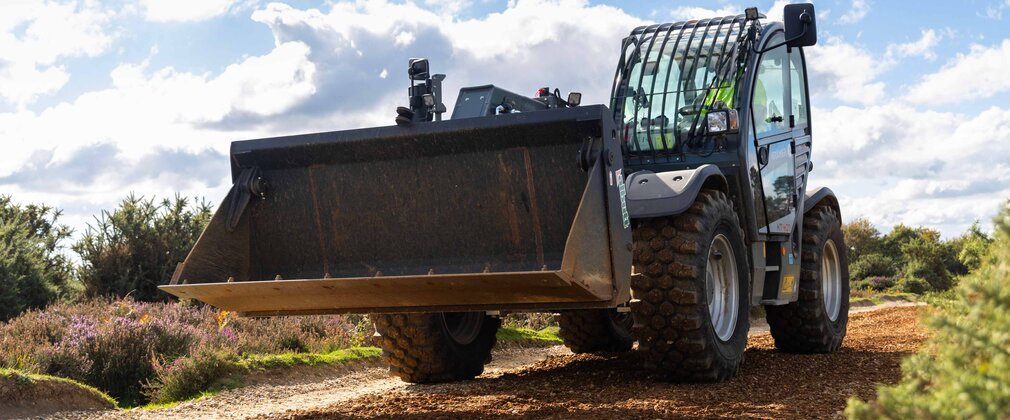 A tractor with a bucket on the front spreading gravel on a track to smooth out the surface.