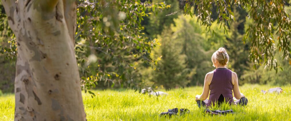 Woman sat on grass in sunshine in yoga pose