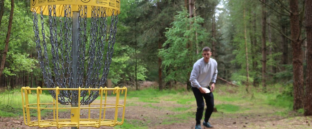 A man holding a flying disc close to a disc golf net in the forest.