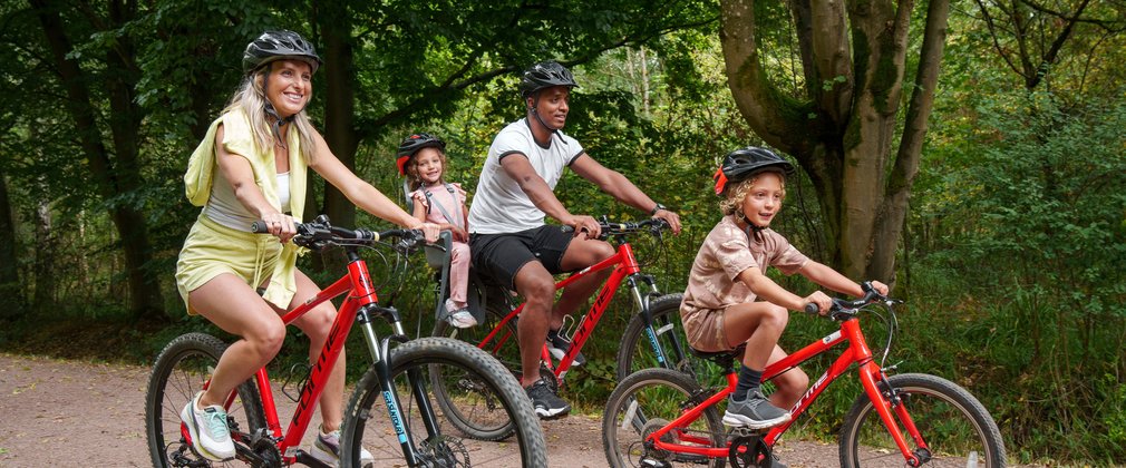 Two adults and two children all riding red bikes on a forest path