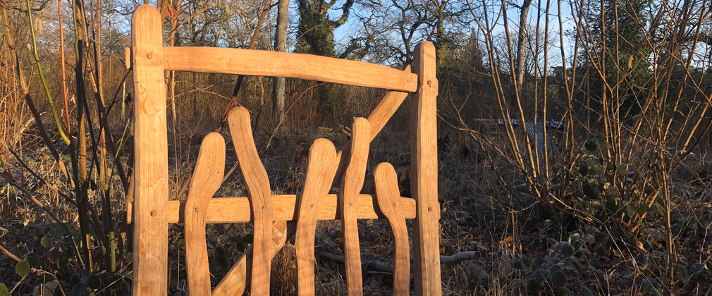 An Oak gate created from an oak gate making course at Westonbirt Arboretum. Light brown intricately cut bits of wood have been formed to make a beautiful gate.