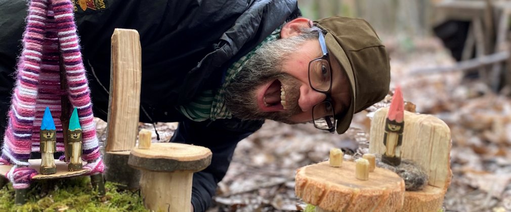 A forest school leader smiling surrounded in green woodworking projects 