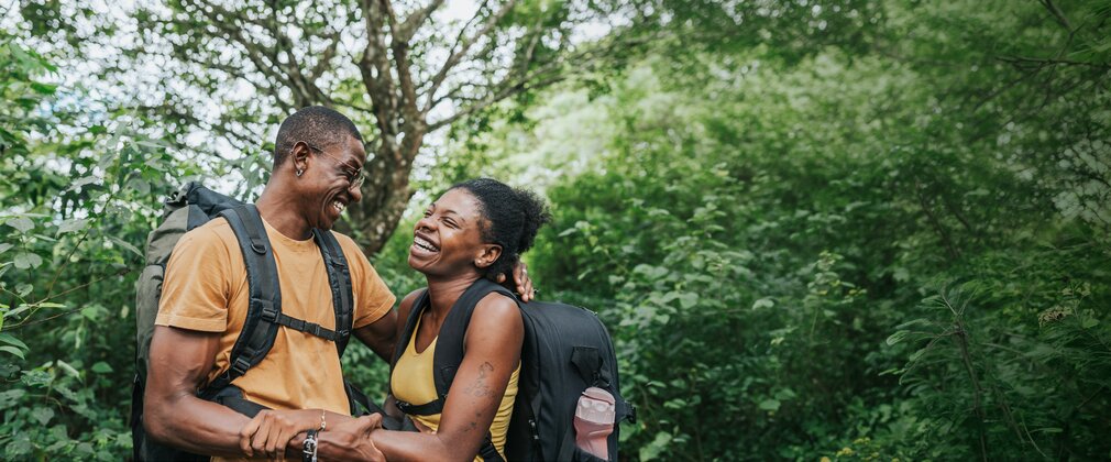 A couple smile at each other while walking through a wooded area