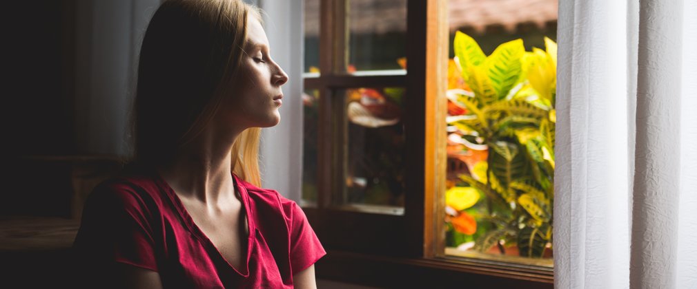 Woman with closed eyes facing out of a window