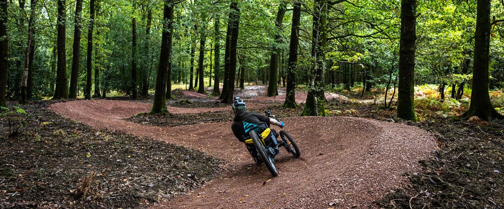A man riding a three-wheeled adapted bike along a trail in a forest.