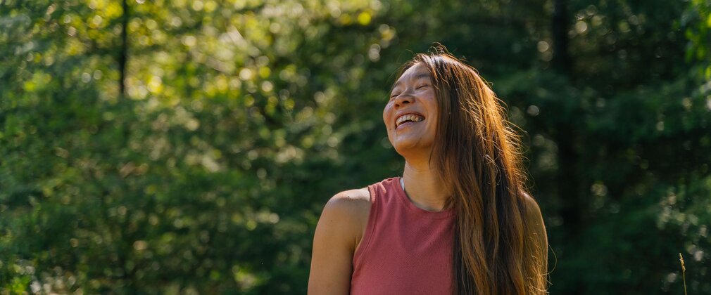 Woman laughing in a sunny forest.