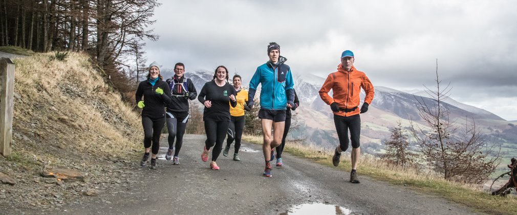 A group of seven runners on a hillside path