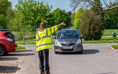A member of the team in a high vis jacket waves a car through to a space in the car park. 