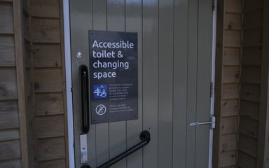 A sage green door with a sign that says 'accessible toilet and changing space' on a black sign