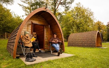 Wooden glamping pod with two people sitting outside reading books