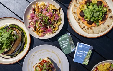 A selection of food on a table surrounding two maps of Grizedale Forest