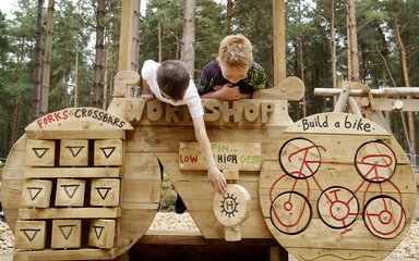 Boys playing on a wooden piece of play equipment shaped like a bike