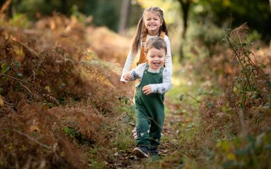 A young girl and boy on a grassy track surrounded by autumnal foliage.