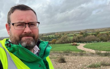 Man in glasses stood in front of woodland