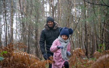 Father chasing daughter through shrubs in wintry forest