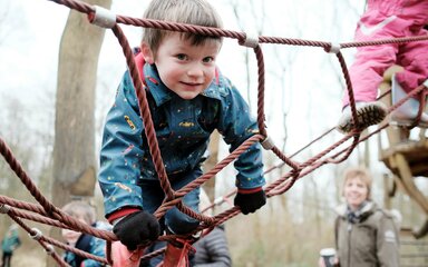 A young boy wearing coat and gloves smiles on a climbing net.