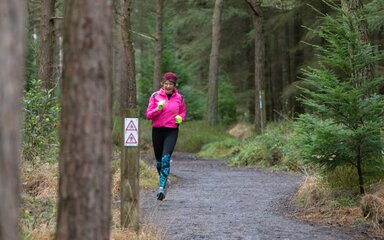 A woman in running clothes and a pink hat running along a forest path in winter